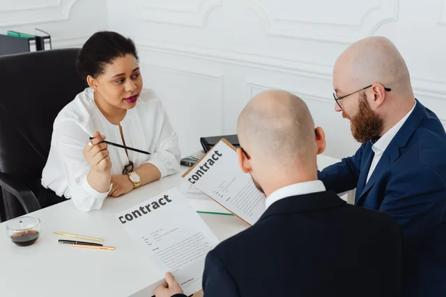 Three business professionals in discussion over a contract in a modern office setting. Inköpsrutiner och leverantörsavtal för mindre bolag